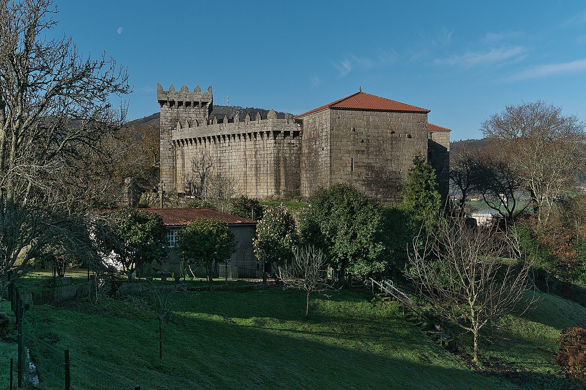 O Castelo de Vimianzo visto desde fóra: muralla ameada, torre da homenaxe e o tellado de tella vermella da vivenda, sobre unha ladeira verde.